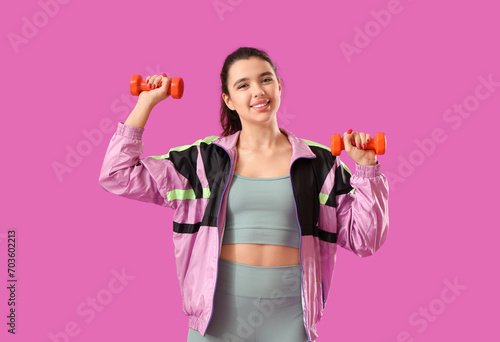 Young woman in sportswear with dumbbells on purple background