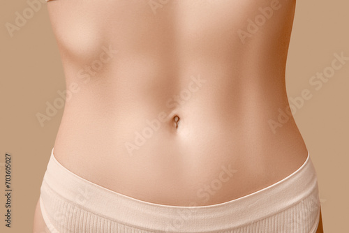 Young woman with flat belly on beige background, closeup. Plastic surgery concept photo