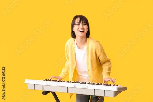 Canvas Print Young woman playing synthesizer on yellow background