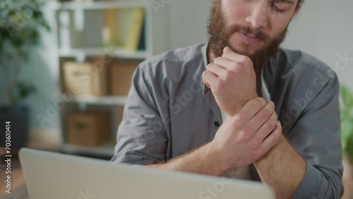 Wrist Pain. A Man Suddenly Feels Pain in her Wrist During Work on Laptop. Touches her Sore Arm With her Other Hand. Office syndrome concept. Hand Pain From Using Keyboard.