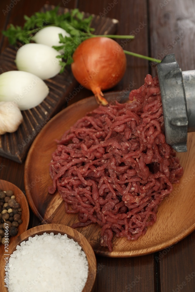 Meat grinder with beef mince, onion, parsley and spices on wooden table Meat grinder with beef mince, onion, parsley and spices on wooden table