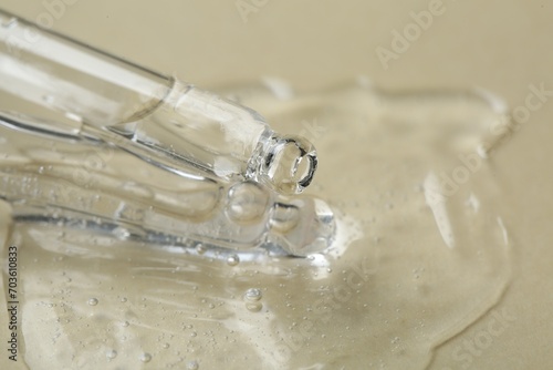 Pipette with cosmetic serum on beige background, closeup