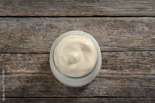 Fresh mayonnaise sauce in glass jar on wooden table, top view