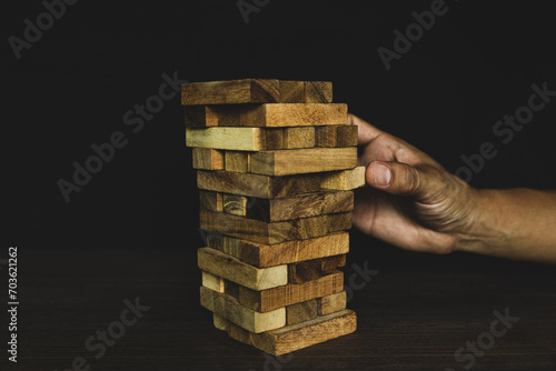 Hand pull wooden block tower stack in pyramid stair step with caution to prevent collapse or crash concepts of financial risk management and strategic planning and business challenge plan.