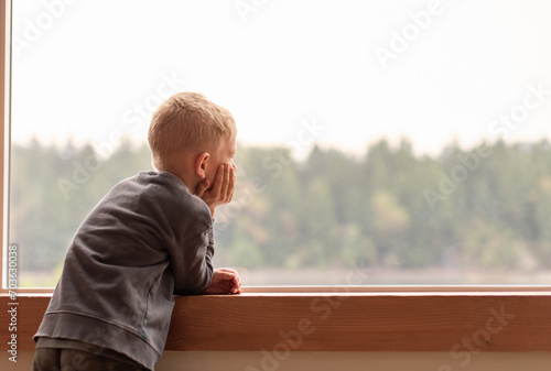 thoughtful alone child at home looking out his window 