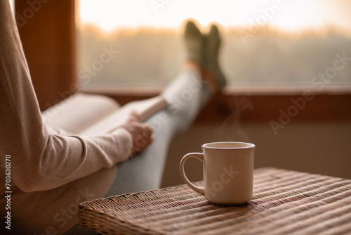 Person relaxing at home reading book feeling relaxed on a cozy winter morning enjoying cup of hot  tea coffee  photo