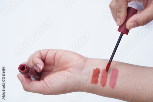 Close up woman hand is testing lip gloss different colors  apply on her arm. Lipstick swatches on hand for colors test or cosmetic allergy test. Make up equipment or tool.            