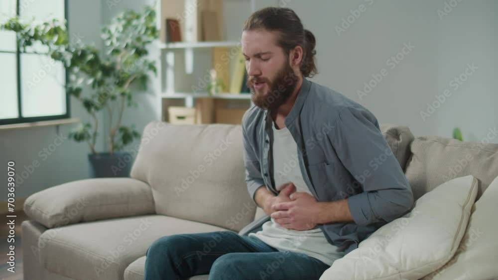 Man sitting on the couch suddenly felt pain in his stomach. Man trying to relieve pain by massaging his stomach Man sitting on the couch suddenly felt pain in his stomach. Man trying to relieve pain by massaging his stomach