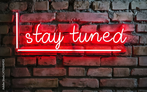 Red neon light text "stay tuned" against brick wall.