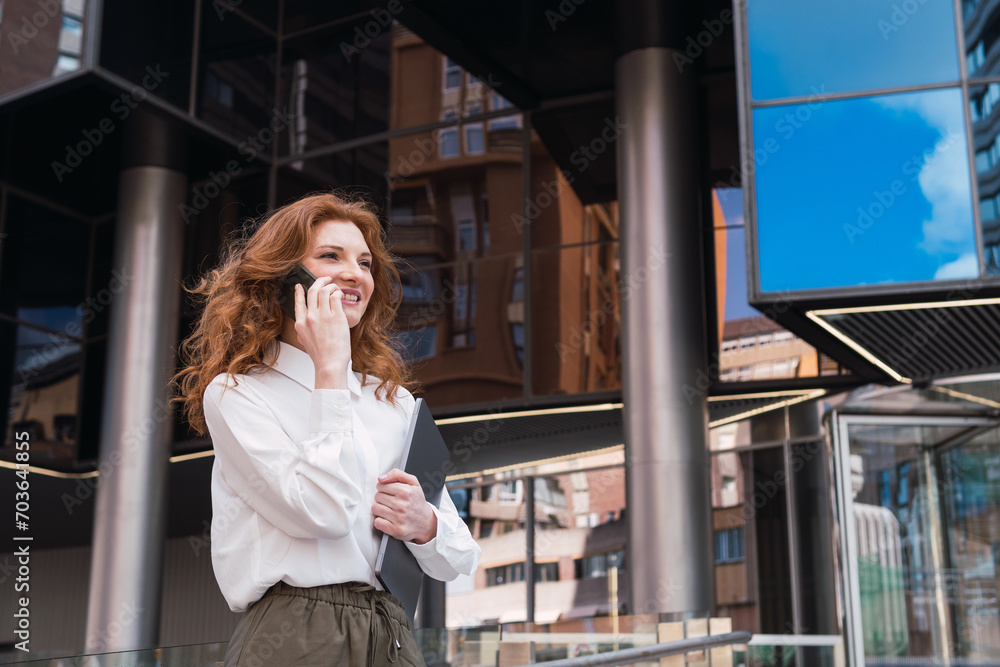 Fototapeta premium Caucasian business woman leaving office with laptop while talking with phone