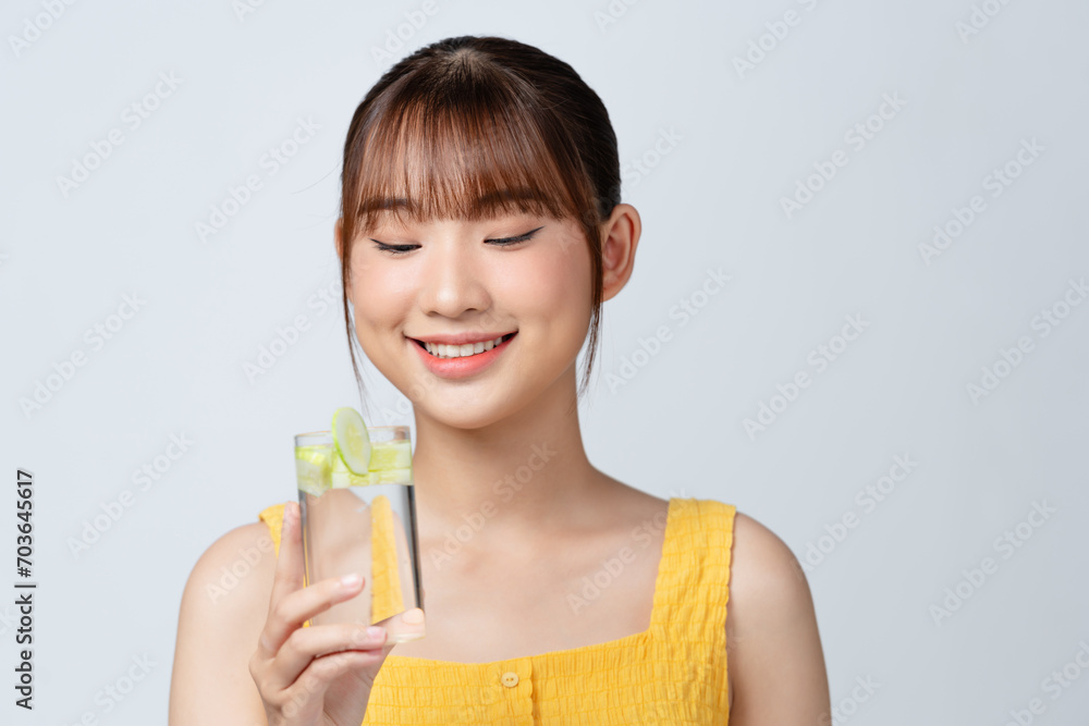 a beautiful young woman with a glass of water with cucumber slices isolated on white. a beautiful young woman with a glass of water with cucumber slices isolated on white.