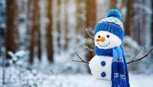 Cute snowman in a blue knitted bobble hat and scarf in a winter forest with copy space.