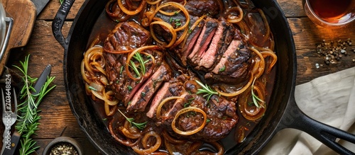 Top view of Filipino dry aged angus bistek tagalog steak with onion rings in soy sauce in a cast-iron casserole. photo