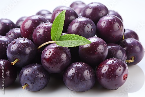 Fresh purple plums with water droplets and a green leaf on a white background.