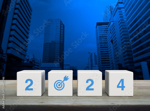 2024 letter with goal icon on white block cubes on wooden table over modern office city tower and skyscraper, Happy new year 2024 success concept