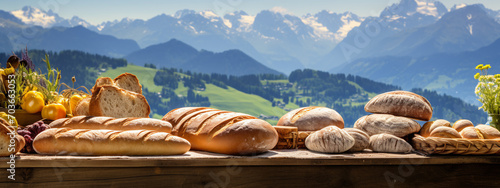 Assortment of fresh bread on a wooden table with the picturesque snow peaks mountains in the background, evoking the essence of artisanal baking. photo