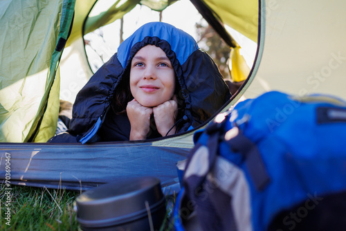 camping and trekking with children. happy smiling child lies in a tent covered with a sleeping bag. portrait of a child in a tent.