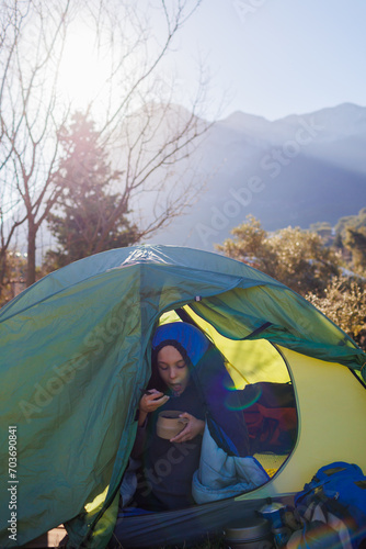 child sits in a tent against the backdrop of the mountains and has breakfast. boy in a sleeping bag with a plate in his hands. portrait of a child in a tent.
