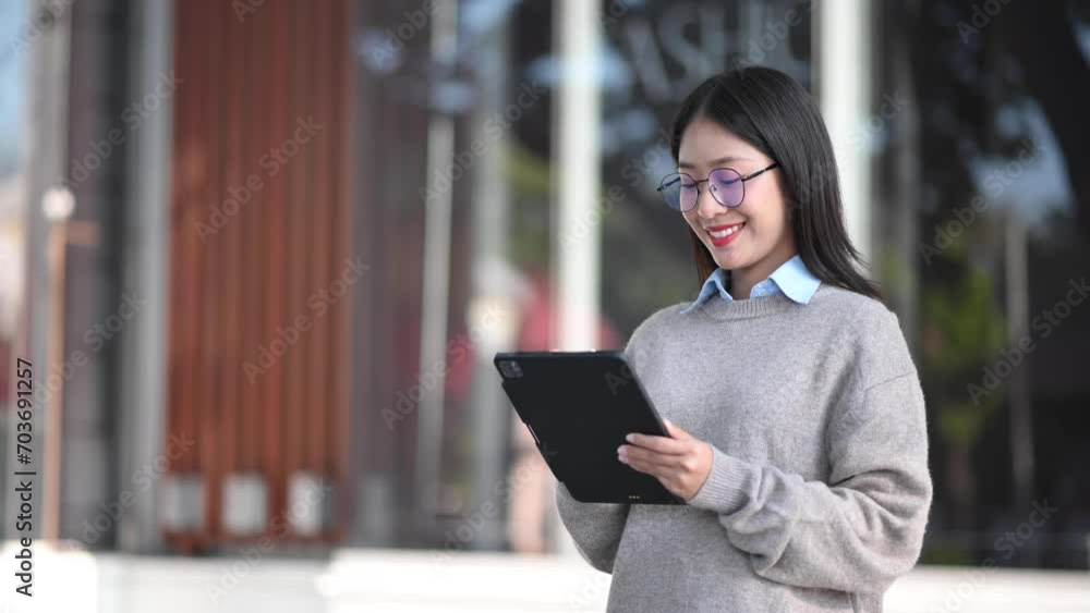 Confident Asian woman with a smile standing holding notepad and tablet at out side office. big city Confident Asian woman with a smile standing holding notepad and tablet at out side office. big city