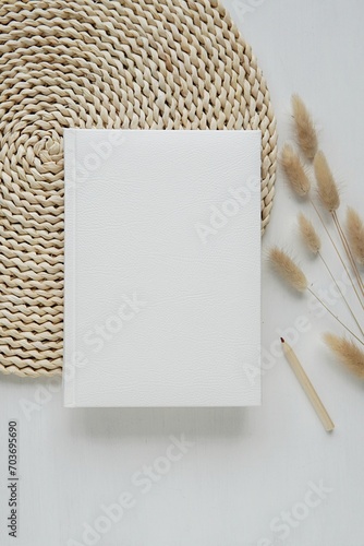 Vertical image with white hard cover notebook mockup for planner, journal, photo album, workbook design, aesthetic flat lay with wicker mat and bunny tail grass.