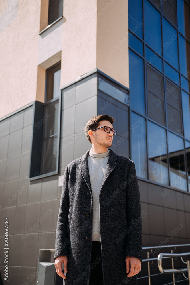 The image depicts a person standing outdoors wearing a black coat and a The image depicts a person standing outdoors wearing a black coat and a