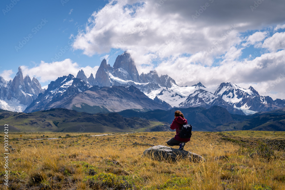 A woman with red cloth taking a picture of Mt.Fitzroy in the yellow field with dramatic clouds and sky (Patagonia, El chalten, Argentina)