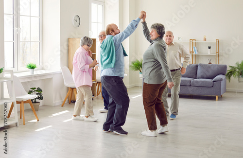 Group of elderly people having a party, dancing and having fun together. Several mature men and women dancing in the living room at home or in a senior care center. Old age, fun, leisure concept photo