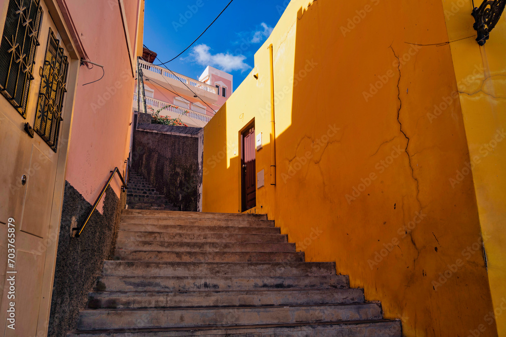 A vibrant stairway scene, with warm yellow walls that frame the ascent, capturing the charming character of Ribeira Grande's street architecture under a bright blue sky.