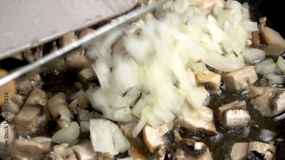 Adding finely diced onions to the mushrooms frying in a frying pan. Slow motion video. Adding finely diced onions to the mushrooms frying in a frying pan. Slow motion video.
