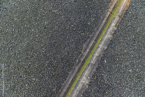 imagen detalle textura suelo asfaltado con una regata para conducir el agua, llena de musgo verde 