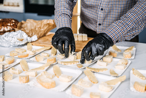Caterer Preparing Cheese Platters for an Event. Professional caterer arranges various types of cheese on plates, wearing gloves for hygiene while preparing for a gourmet event. photo