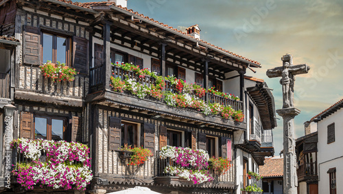 Cruz de piedra del siglo XVIII y hermosa arquitectura tradicional con balcones adornados con macetas y tiestos en la villa medieval de La Alberca, España