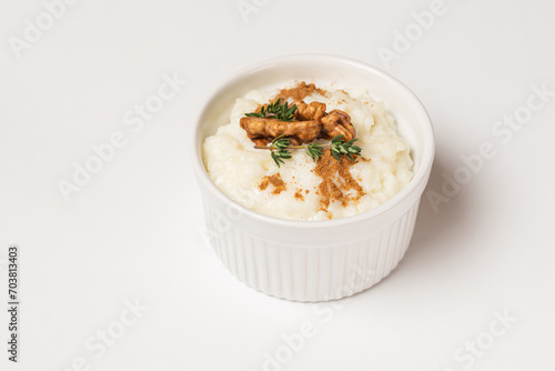 Isolated creamy rice pudding sprinkled in the cinnamon powder and top with walnuts and thyme in a white form on a white background