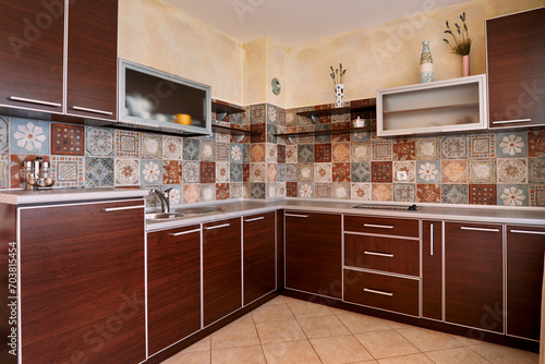Brown furniture in the kitchen with mosaic colorful tiles on the walls