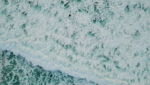 Aerial foaming sea water splashing rolling in slow motion. Surfer swimming ocean