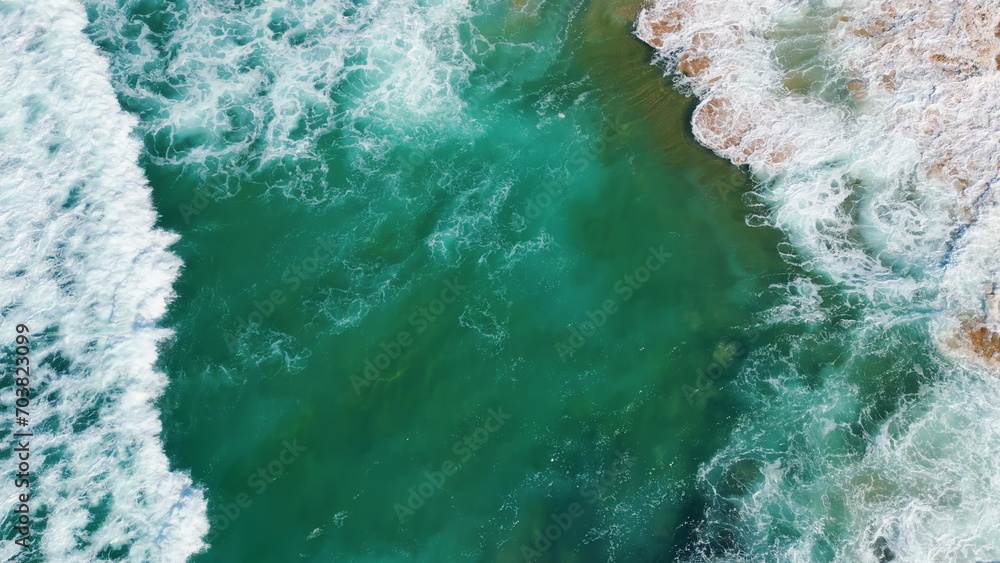 Drone view powerful waves rolling on beautiful sandy beach with volcanic cliffs.