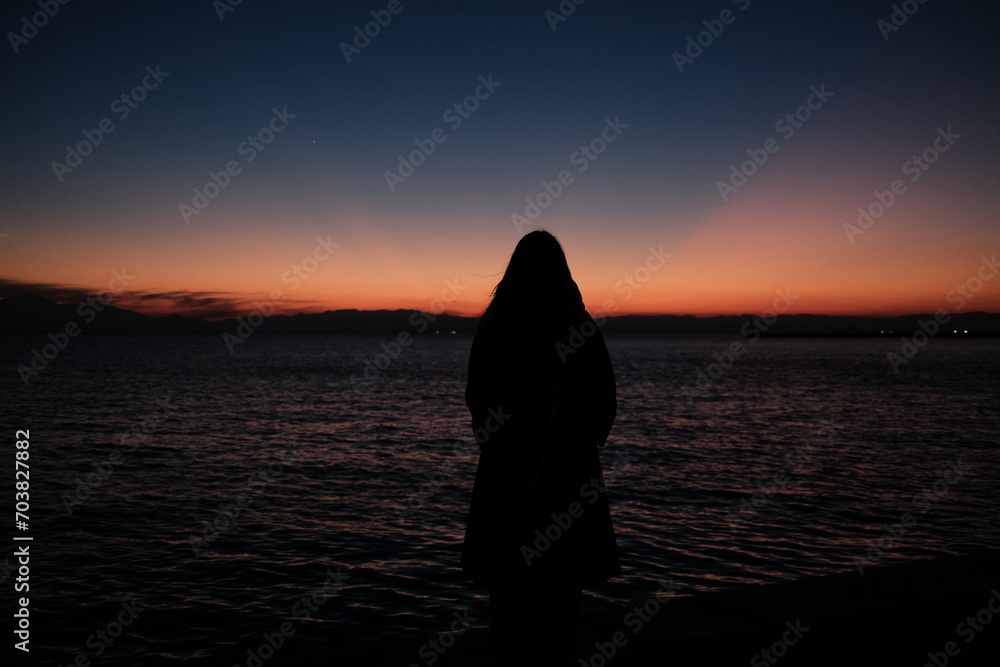A girl watching the sun set over the sea in thessaloniki, Greece.