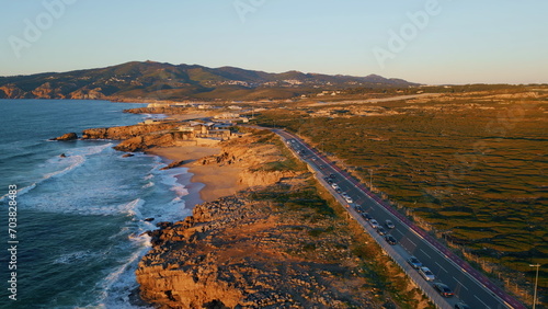 Cars driving coastal road at golden sunlight aerial view. Roadway along seashore