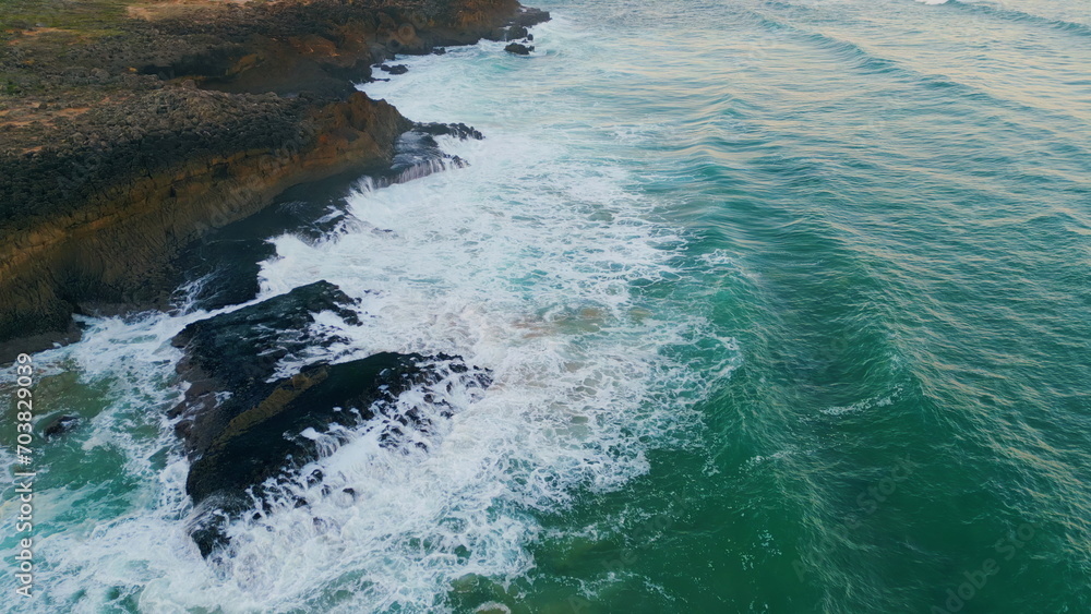 Beautiful foaming blue ocean splashing on rocky coast. Aerial view rough waves.