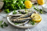 Sardines, lemon, greenery and salt on white plate on marble kitchen table. Mediterranean cuisine