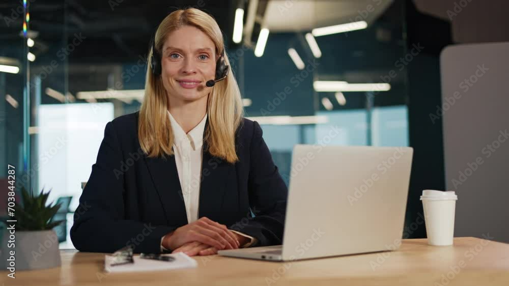 Smiling corporate call center agent with a wireless headset, assisting clients and addressing complaints. Professional telesales woman working in office, looking directly at camera in a webcam view. Smiling corporate call center agent with a wireless headset, assisting clients and addressing complaints. Professional telesales woman working in office, looking directly at camera in a webcam view.