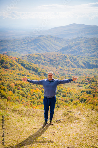 Happy man standing on the background of autumn mountains with arms outstretched to the sides