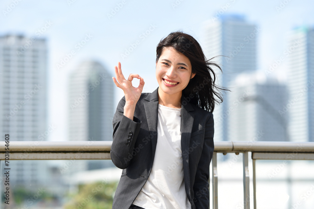 街中でOKサインをするアジア人のビジネスウーマン
