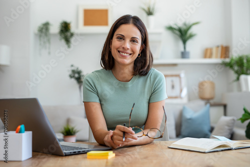 Beautiful business woman working with laptop while looking at camera in living room at home. photo