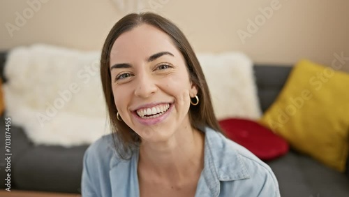Cheerful portrait of a confident young hispanic woman joyfully sticking her tongue out while relaxing on her indoor home sofa. photo