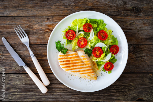 Grilled chicken breast and fresh vegetables on wooden table