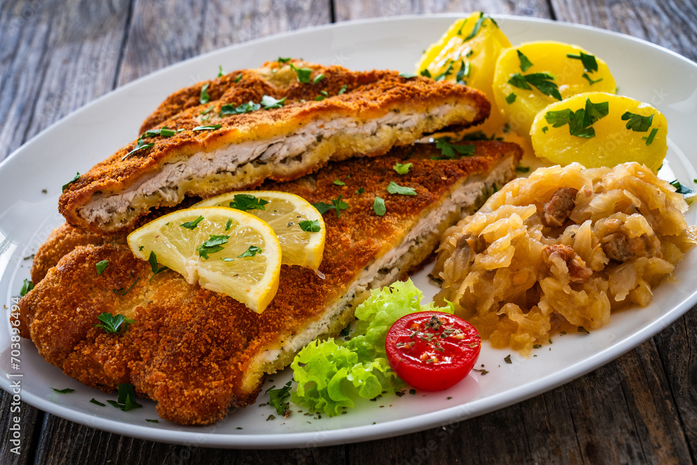 Crispy breaded fried cutlet with boiled potatoes and cooked cabbage on wooden table
Crispy breaded fried cutlet with boiled potatoes and cooked cabbage on wooden table