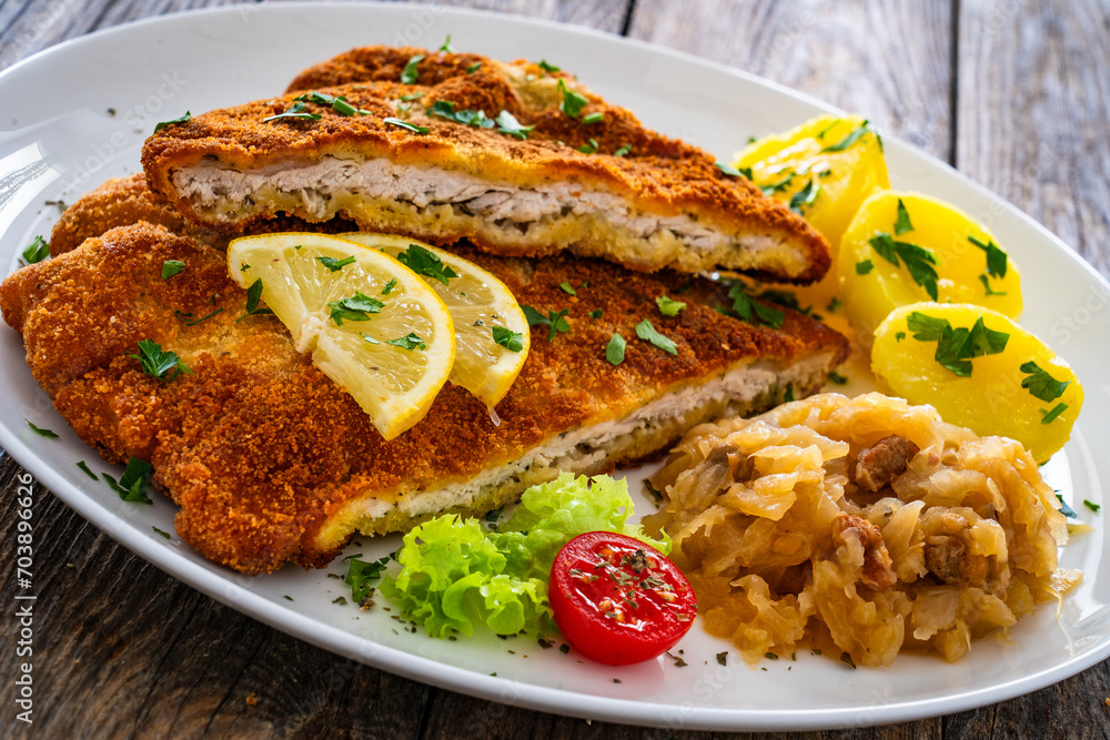 Crispy breaded fried cutlet with boiled potatoes and cooked cabbage on wooden table
