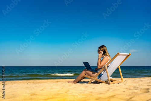 Mid adult woman using laptop and smartphone on beach
 #703899268