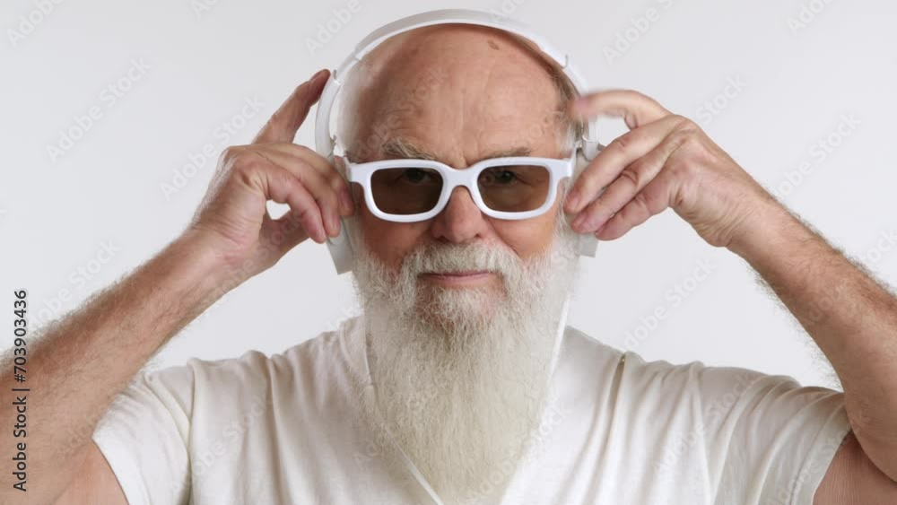 Elderly stylish man in white sunglasses and headphones, with a prominent white beard, set against a white background. His appearance epitomizes grace and elegance at an advanced age. RED 8K RAW. Elderly stylish man in white sunglasses and headphones, with a prominent white beard, set against a white background. His appearance epitomizes grace and elegance at an advanced age. RED 8K RAW.